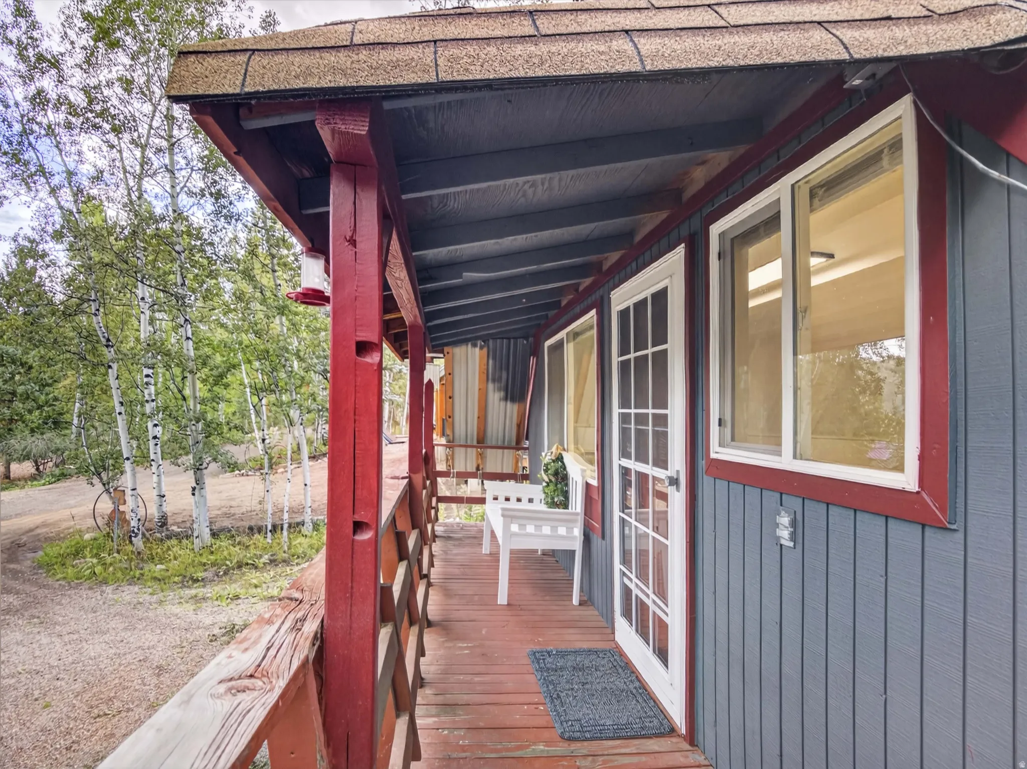 Covered porch with wood flooring and railing, multiple windows, and a glass-paneled entry door