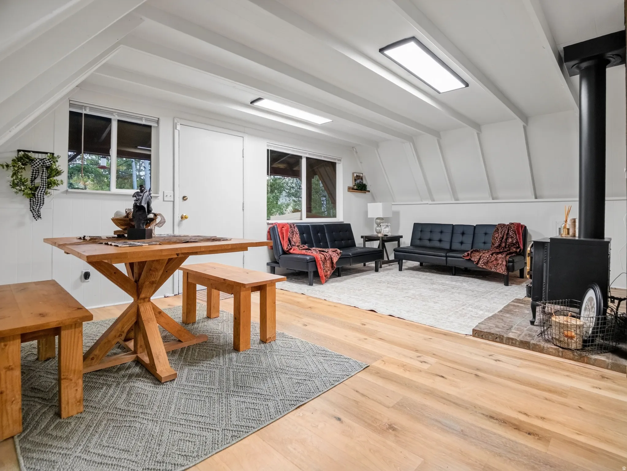 Sloped ceiling with exposed beams, wood-finish flooring, recessed lighting, and a black wood-burning stove with a brick hearth
