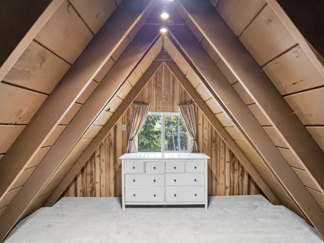 Vaulted ceiling with exposed wood beams, wood-paneled walls, and soft carpeting
