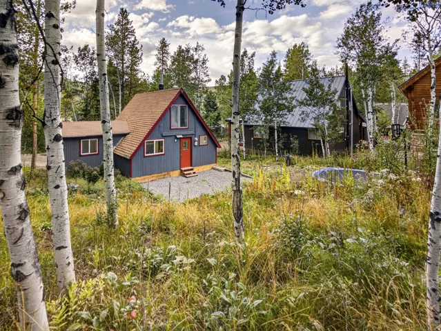 Charming A-frame structure featuring blue siding, red trim, a red entry door, and a brown shingle roof