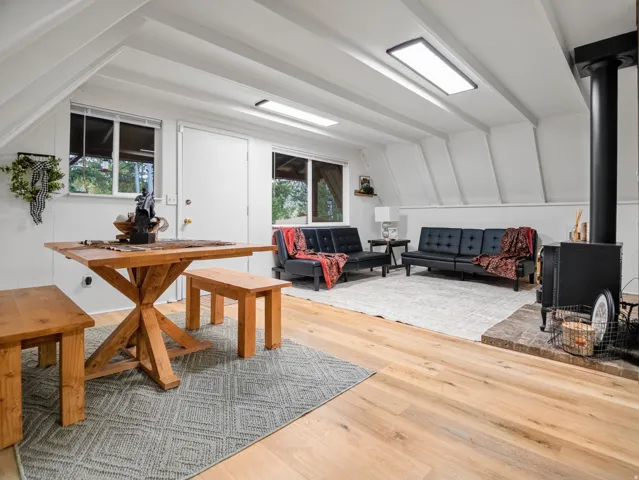 Sloped ceiling with exposed beams, wood-finish flooring, recessed lighting, and a black wood-burning stove with a brick hearth