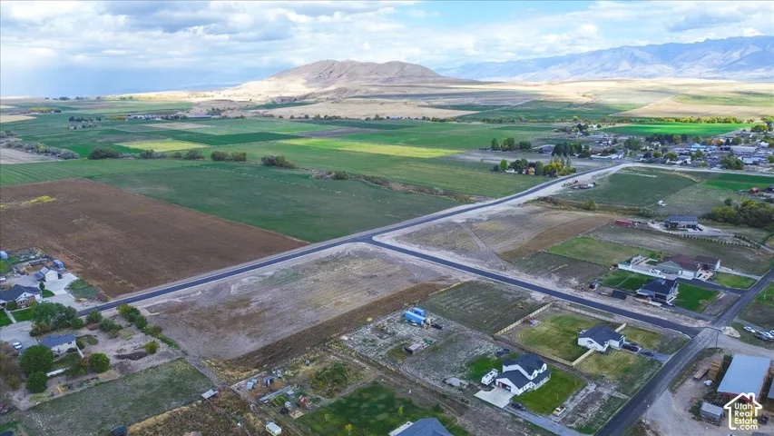 Aerial perspective of expansive open land featuring paved road frontage and mountain backdrops