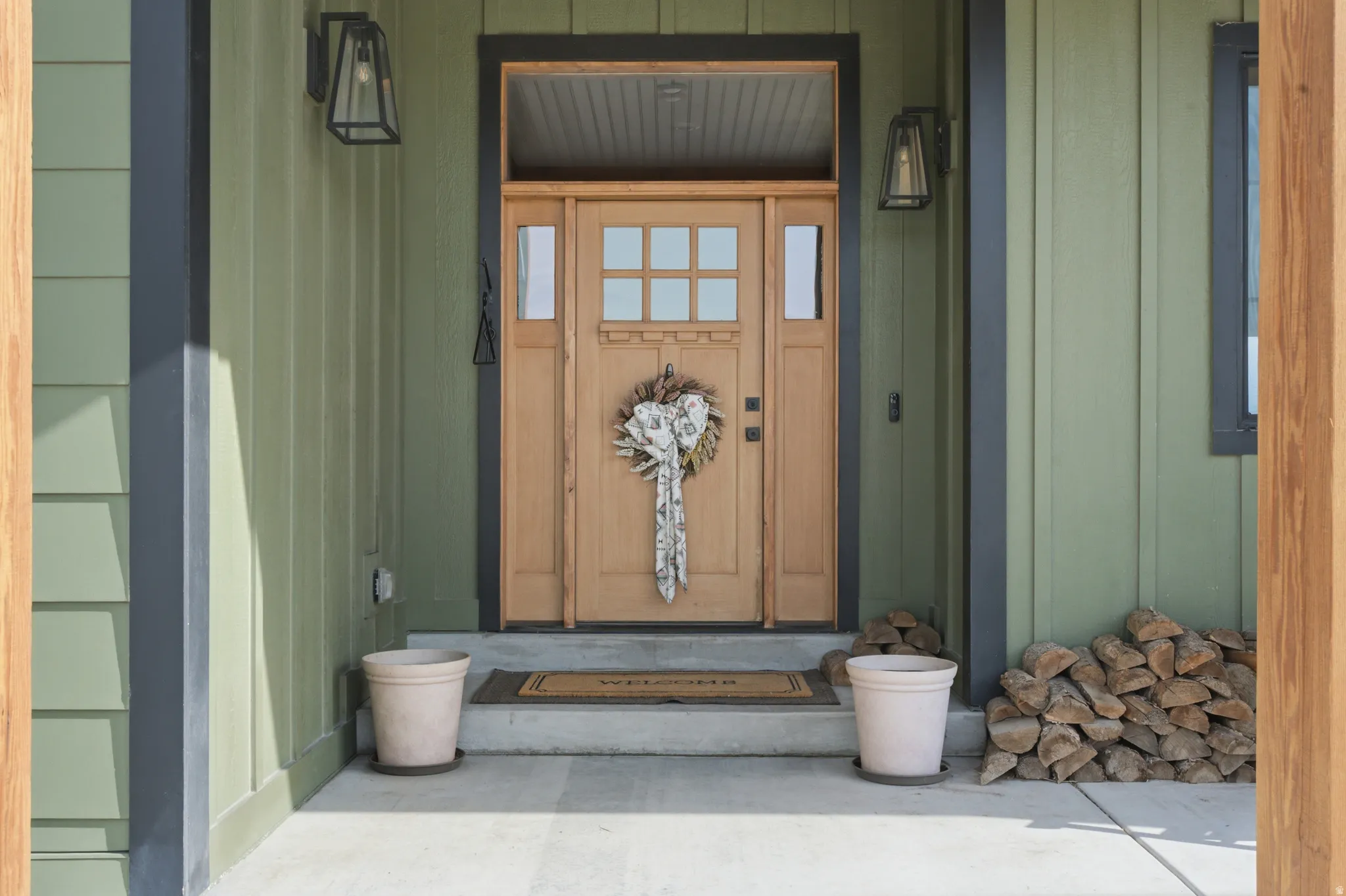 Wood-paneled entry door with sidelights, transom window, and two exterior sconce lights
