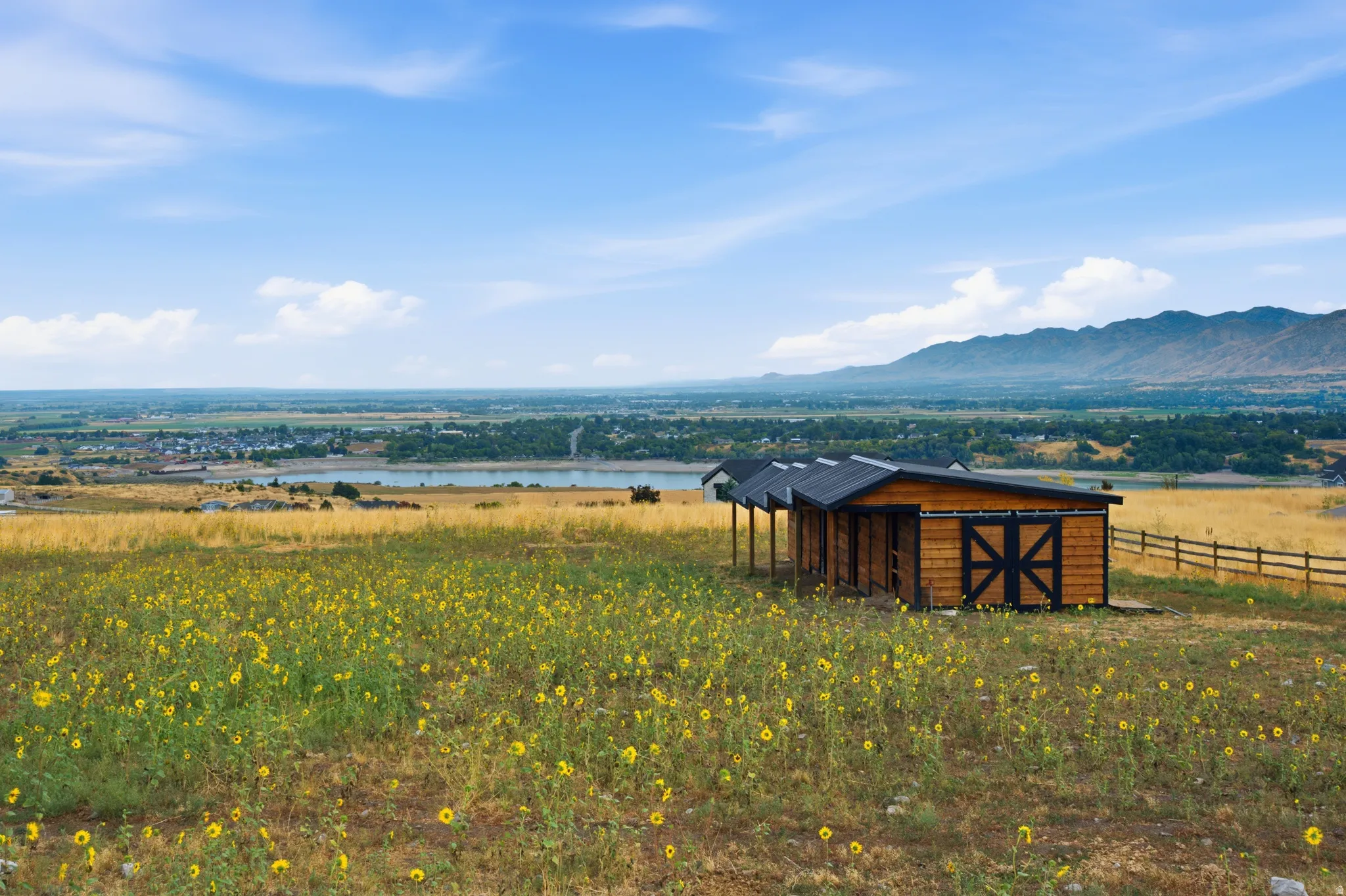Wood-clad outbuilding with covered stalls and a sliding barn door, set amidst a sprawling field