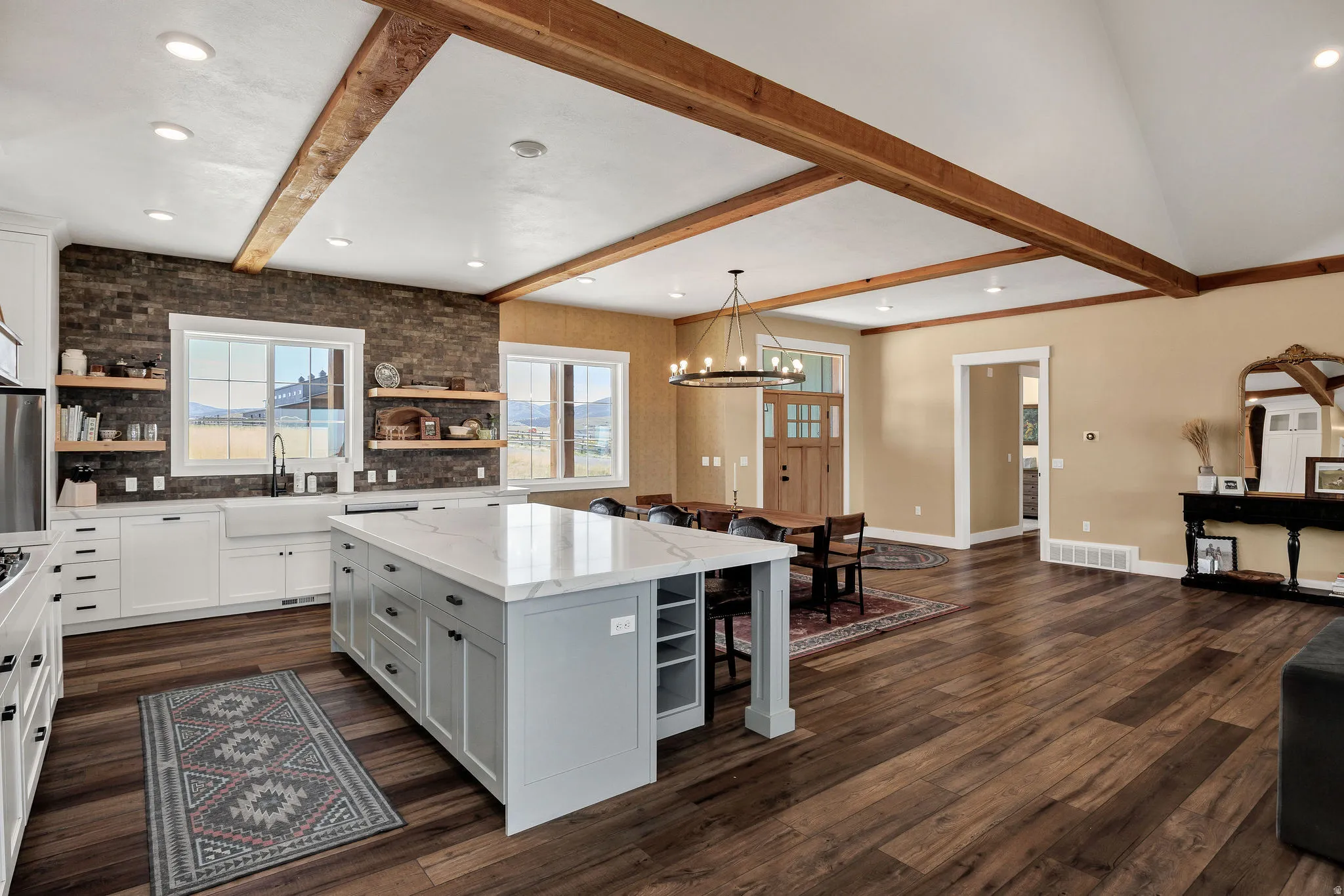 Gourmet kitchen with a large island, white shaker cabinetry, farm sink, and exposed wood beams