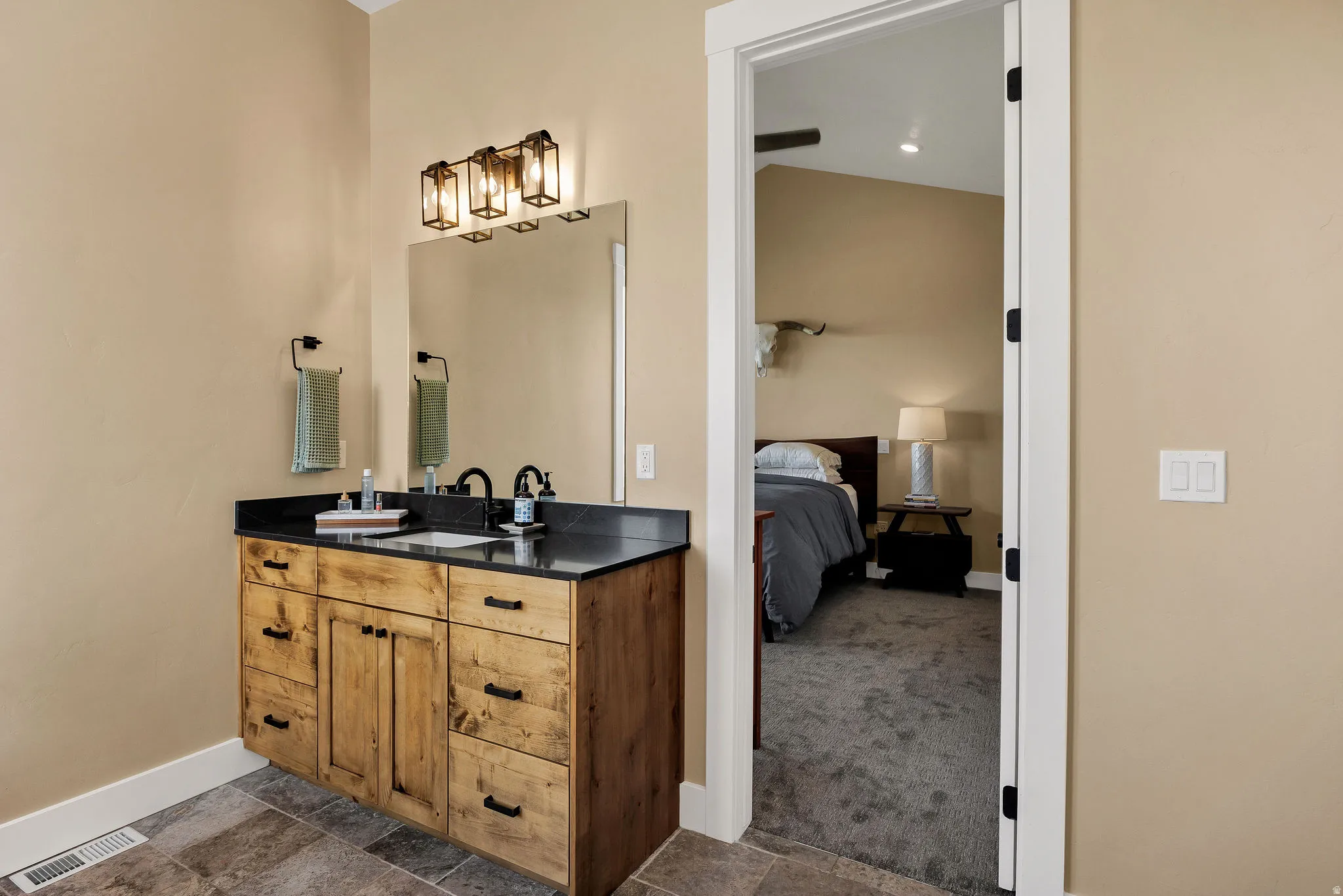 Wood-finish vanity with black countertop and integrated sink, complemented by a three-light vanity fixture