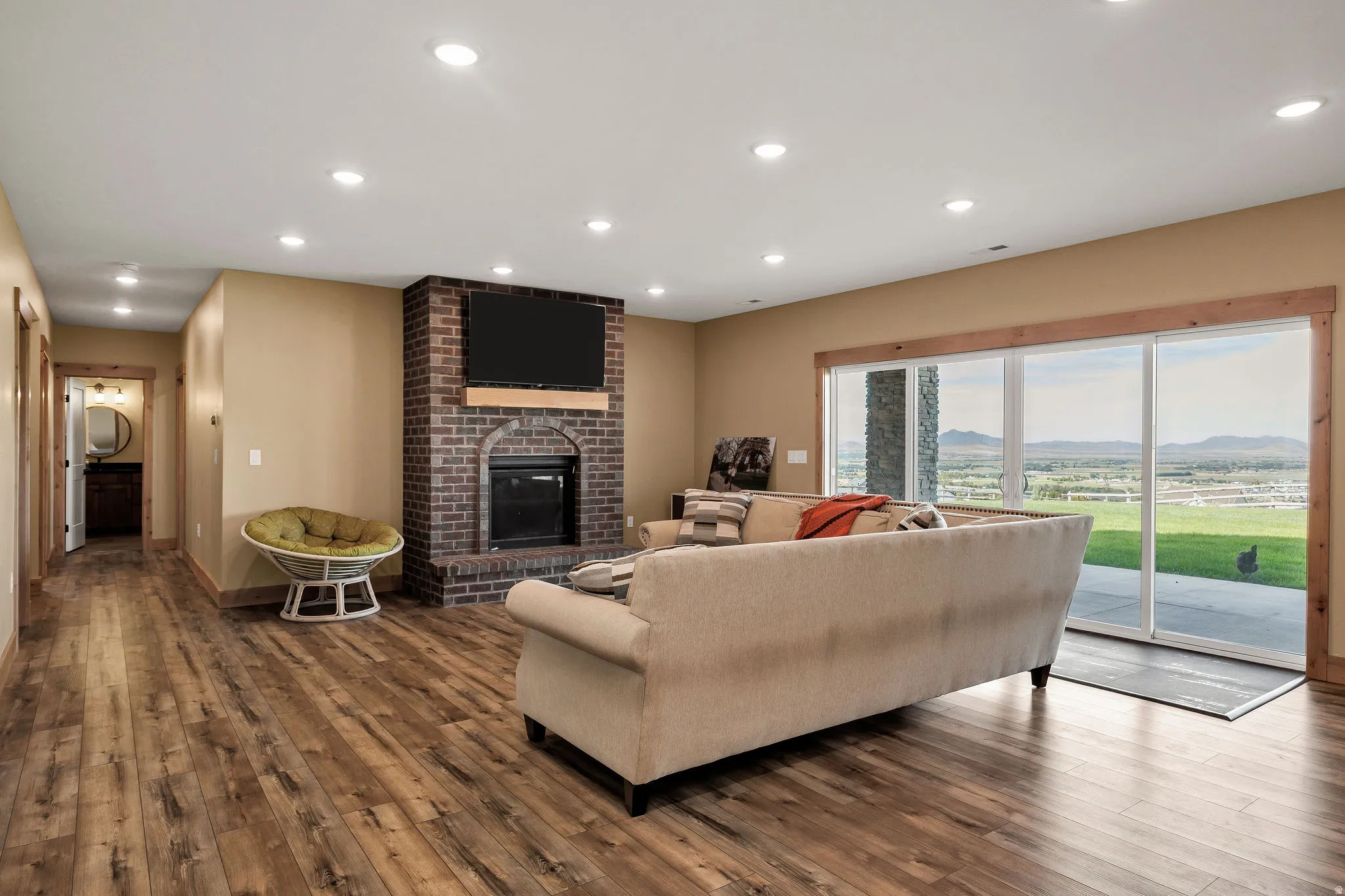 Wood-finish flooring, recessed lighting, brick-clad fireplace with mantel, and large sliding glass doors