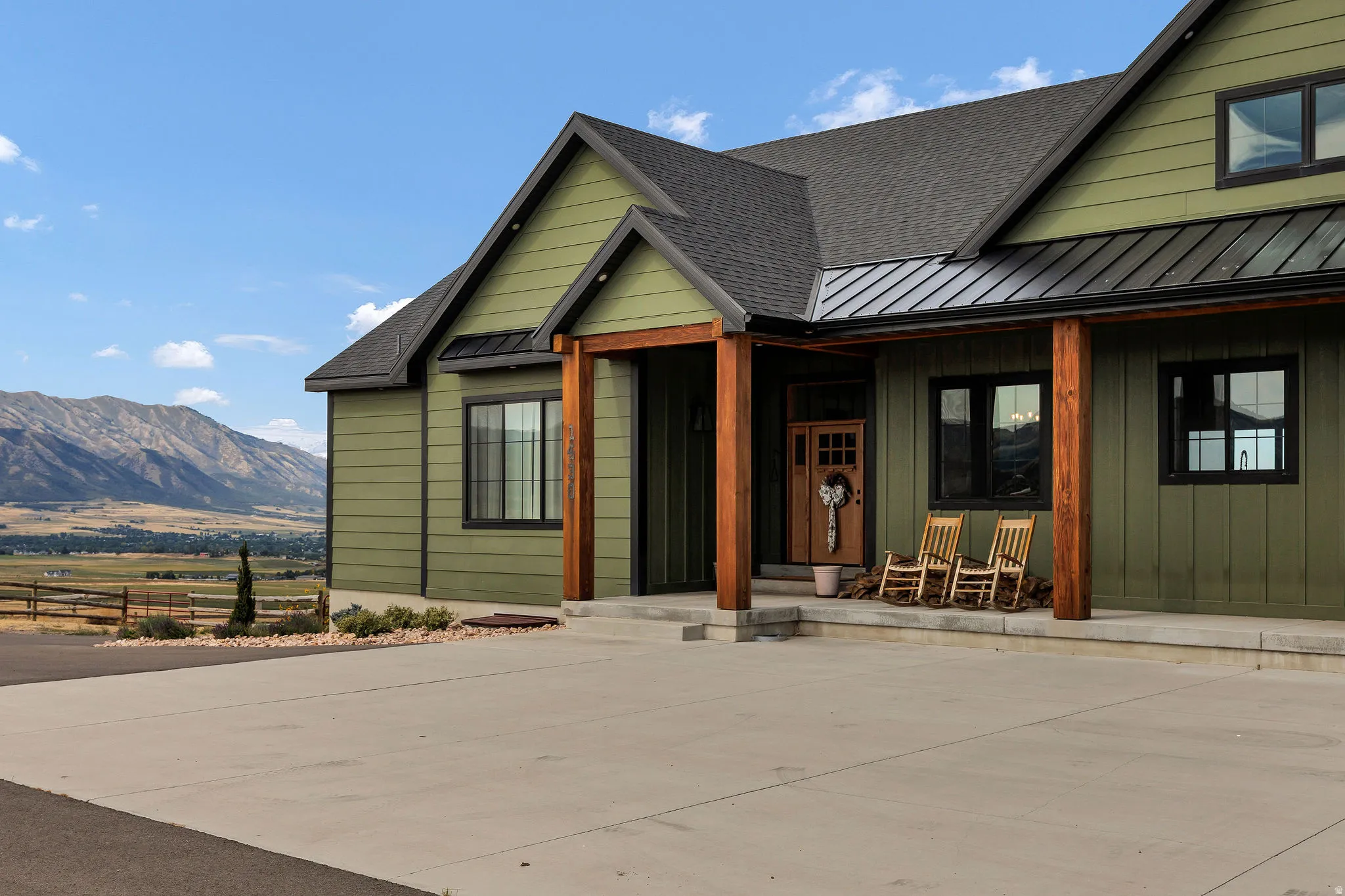 Green horizontal siding exterior with a black shingle roof, black metal roofing, and natural wood support columns