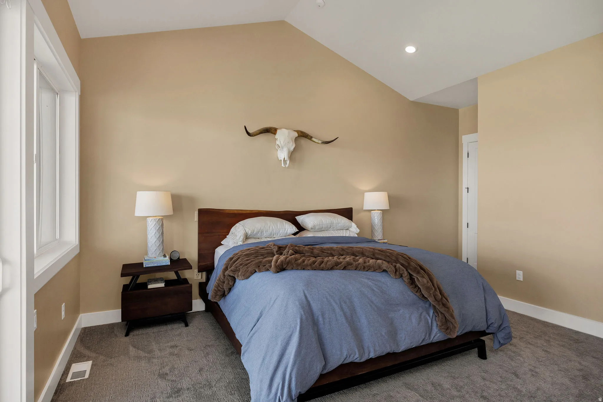 Vaulted ceiling, recessed lighting, white trim window, wood-finish bed frame, light-colored walls