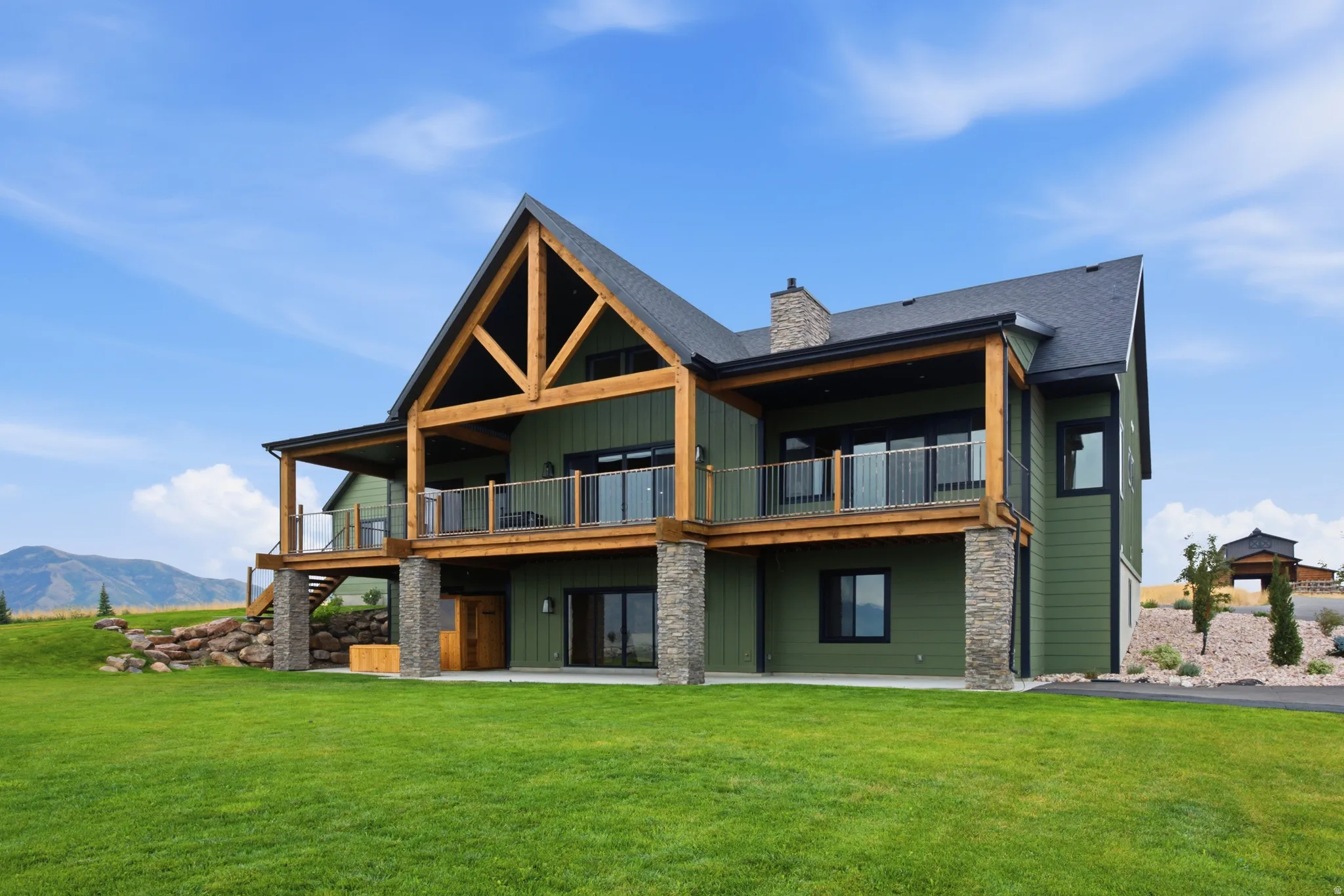 Expansive green siding home with a dark shingled roof, exposed timber framing, stone column accents, and multiple upper-level balconies