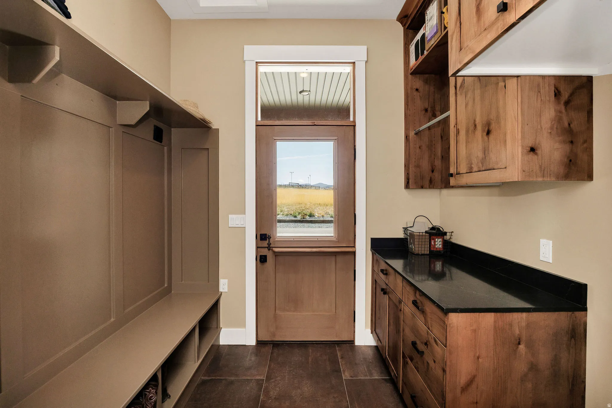Built-in bench with storage, wood-finish flooring, wood cabinetry with dark countertops, and a Dutch door with transom window