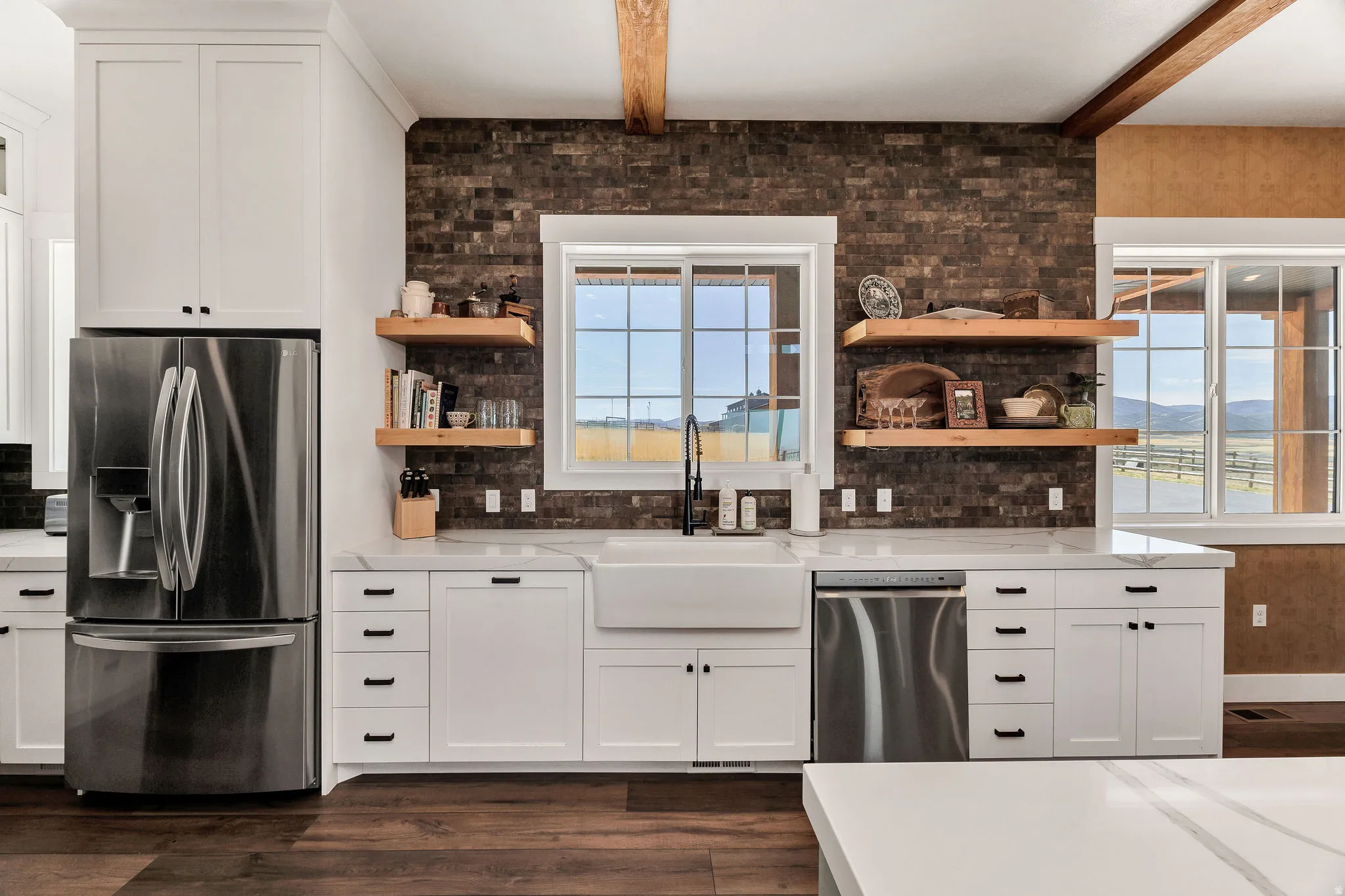 White shaker cabinetry, stainless steel appliances, brick-patterned wall, wood-finish flooring, and a farmhouse sink