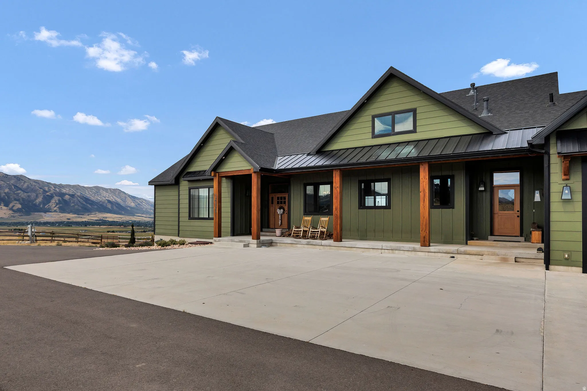 Contemporary-style exterior with green siding, dark trim windows, and a covered front porch with natural wood columns