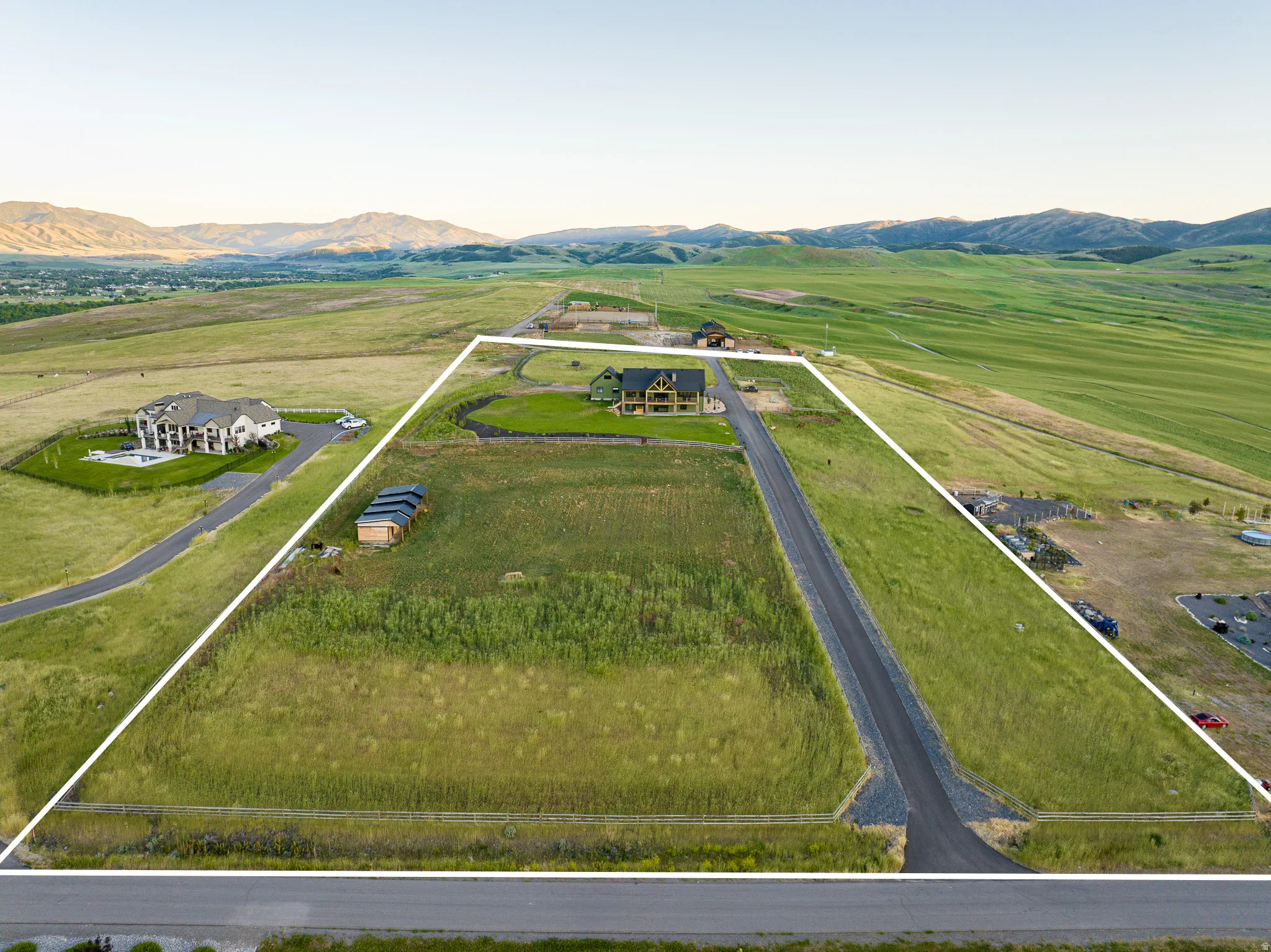 Expansive land parcel featuring a paved road, mountain backdrop, and surrounding green spaces