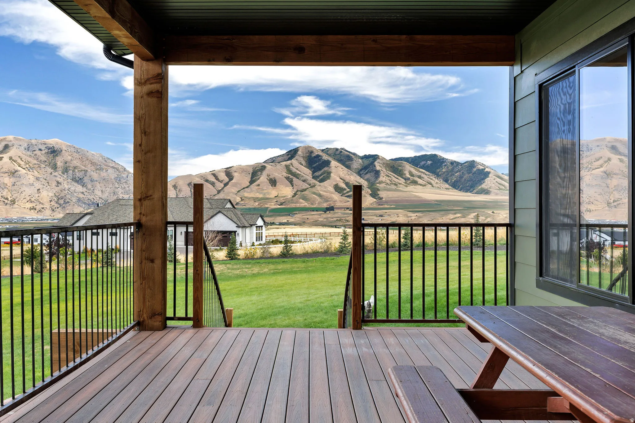 Expansive outdoor deck with wood-finish flooring, featuring a black metal railing and natural wood structural beams