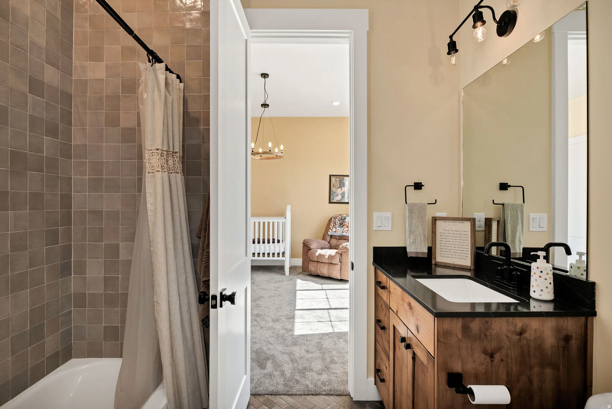 Wood-finish vanity with a black countertop and rectangular undermount sink, complemented by a large wall-mounted mirror and track lighting