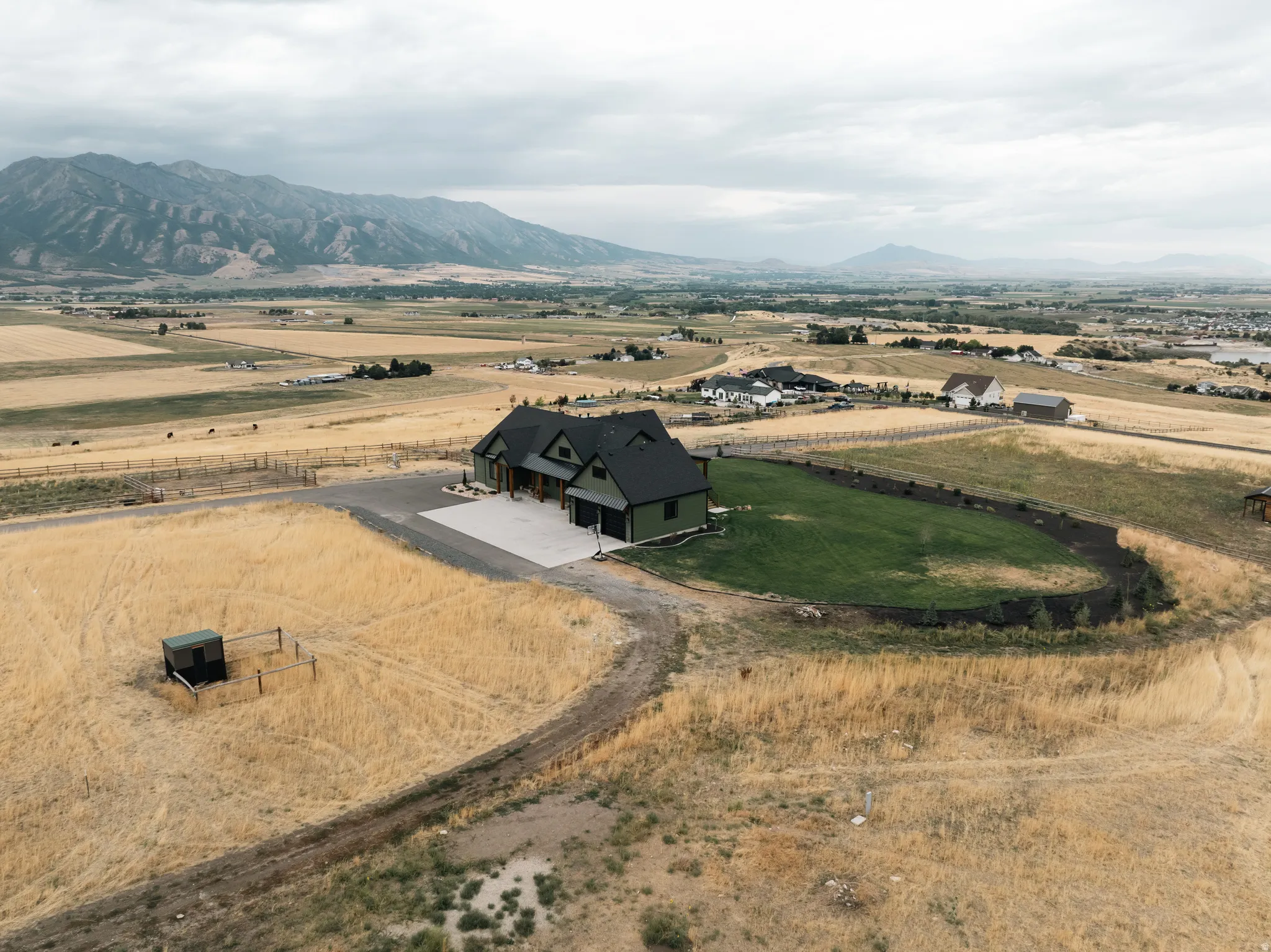 Expansive property featuring a contemporary residence with a dark roof and light siding, surrounded by a large cultivated area and natural terrain