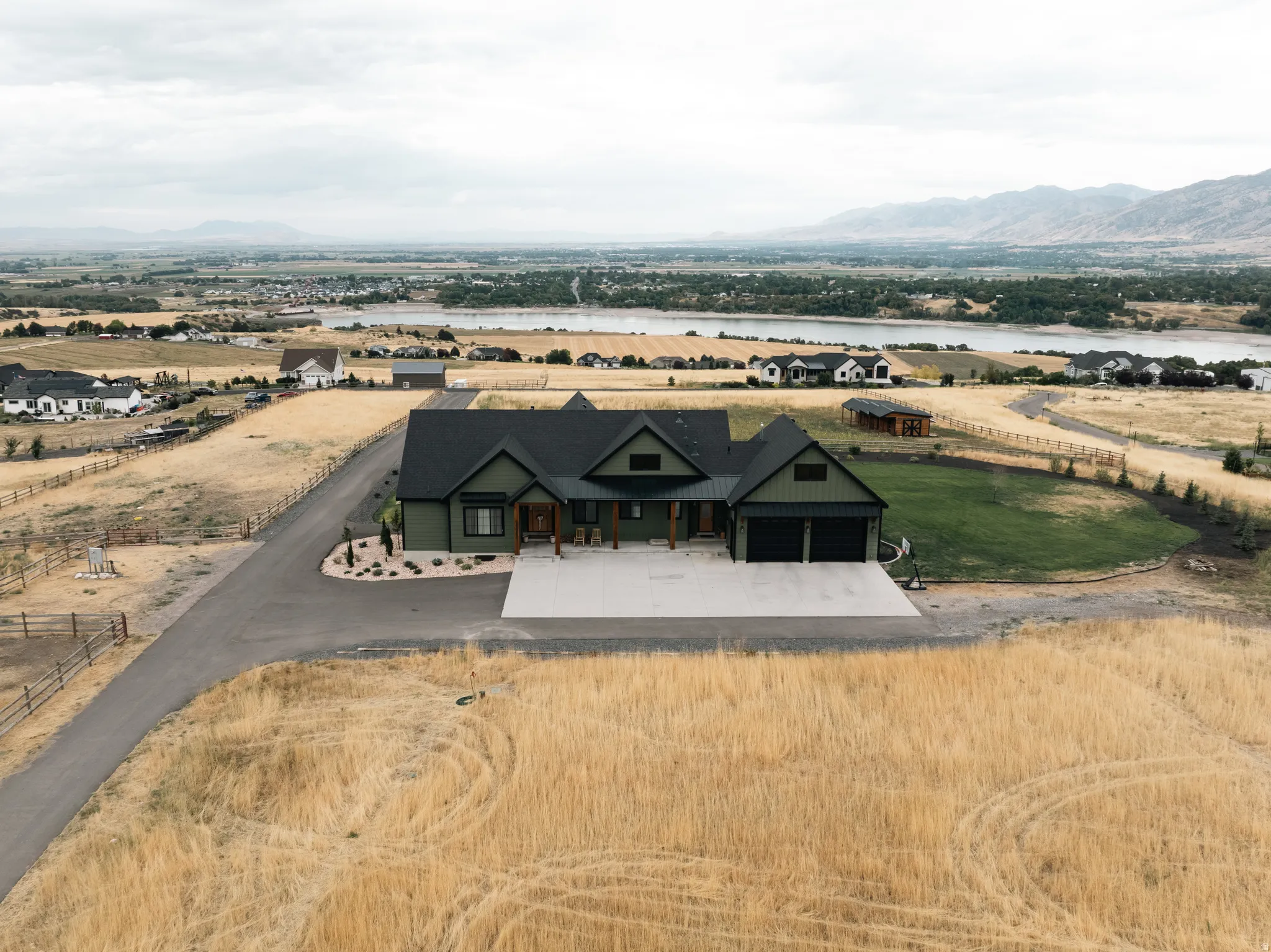 Modern farmhouse exterior with a multi-gabled roofline, attached two-car garage, expansive concrete driveway, and a paved private drive