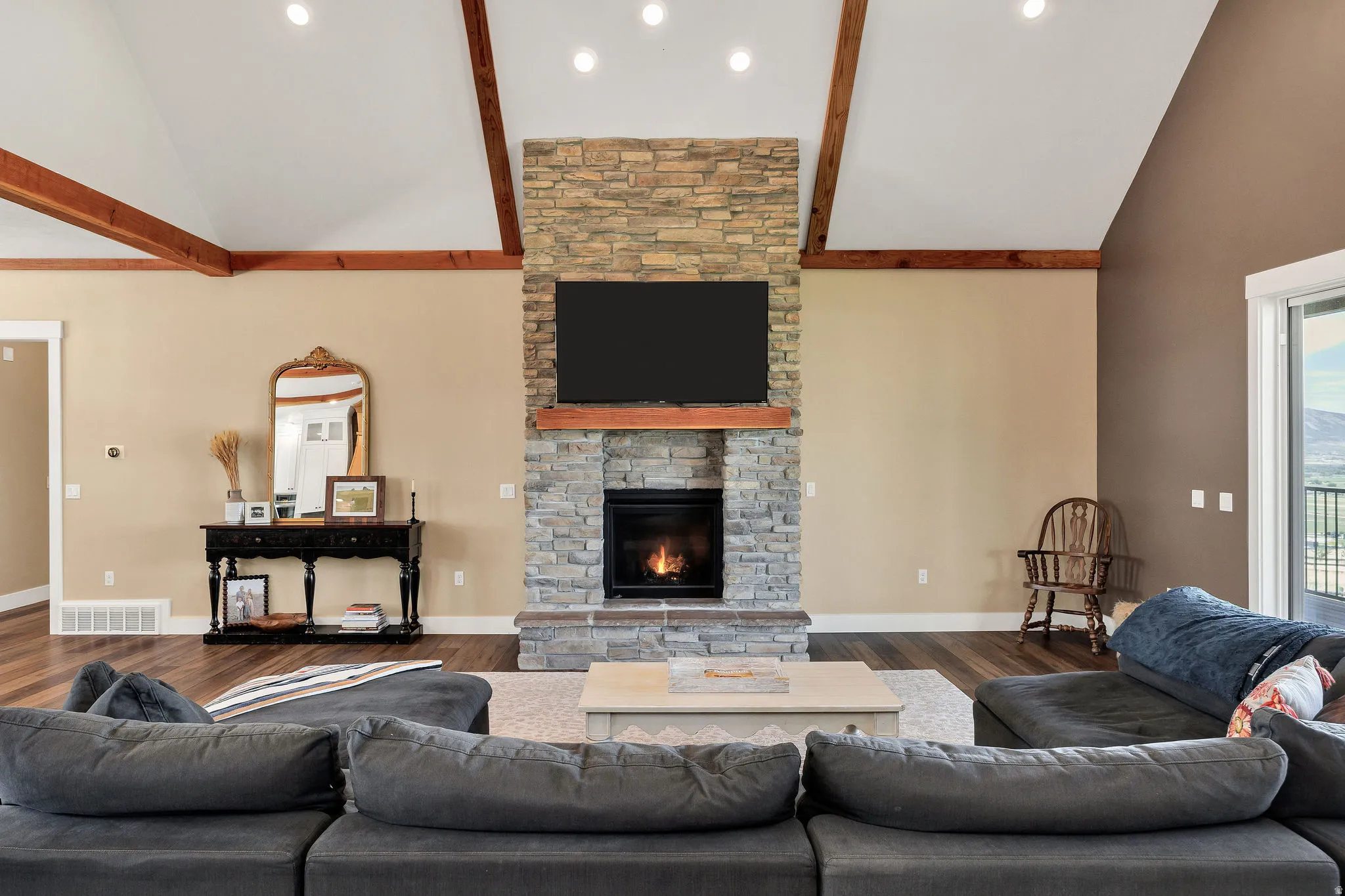 Vaulted ceilings with exposed wood beams, a stone-clad fireplace, and wood-finish flooring