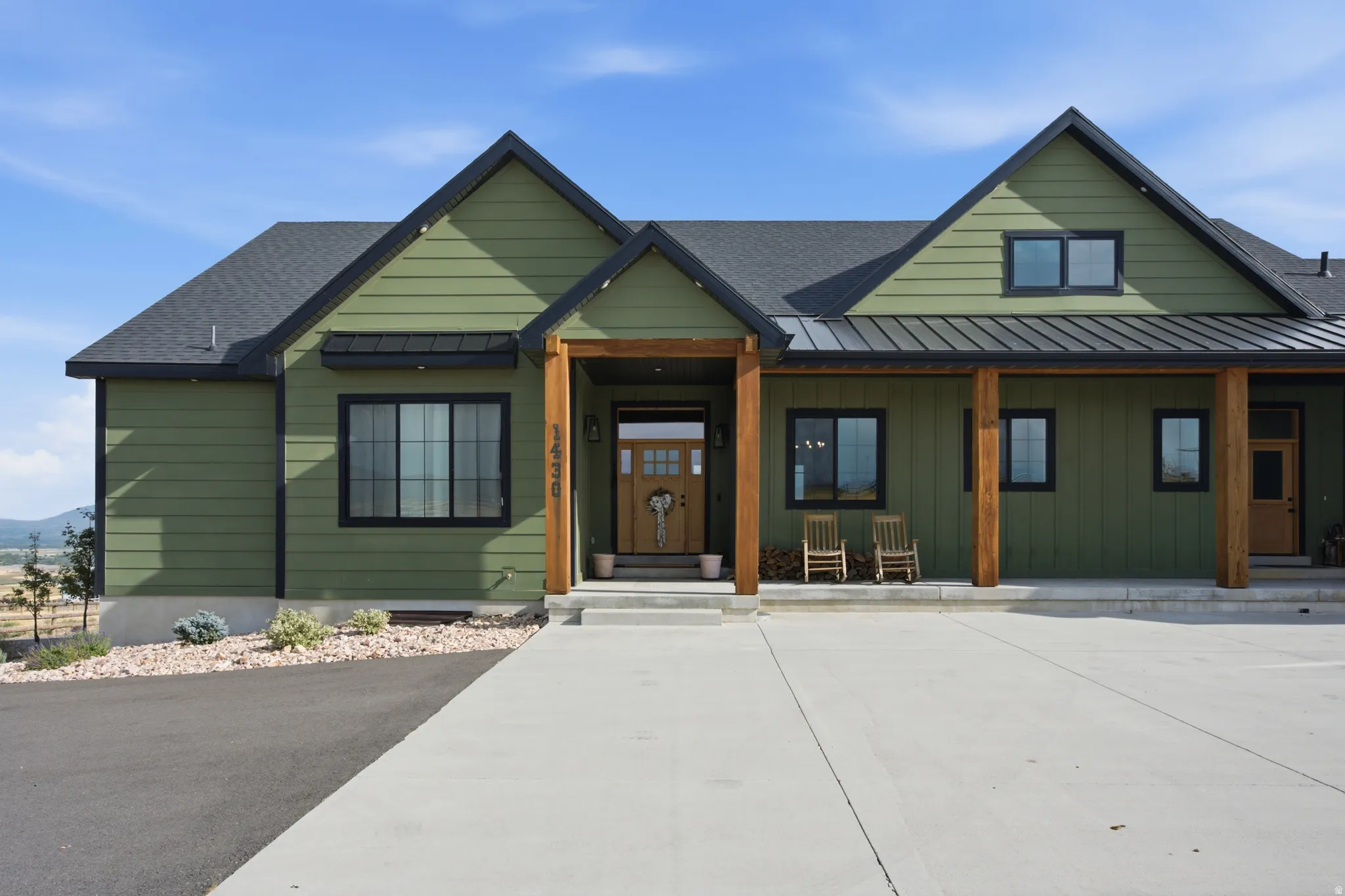 Green horizontal siding exterior with black window frames, a dark shingle roof, and a wood entry door