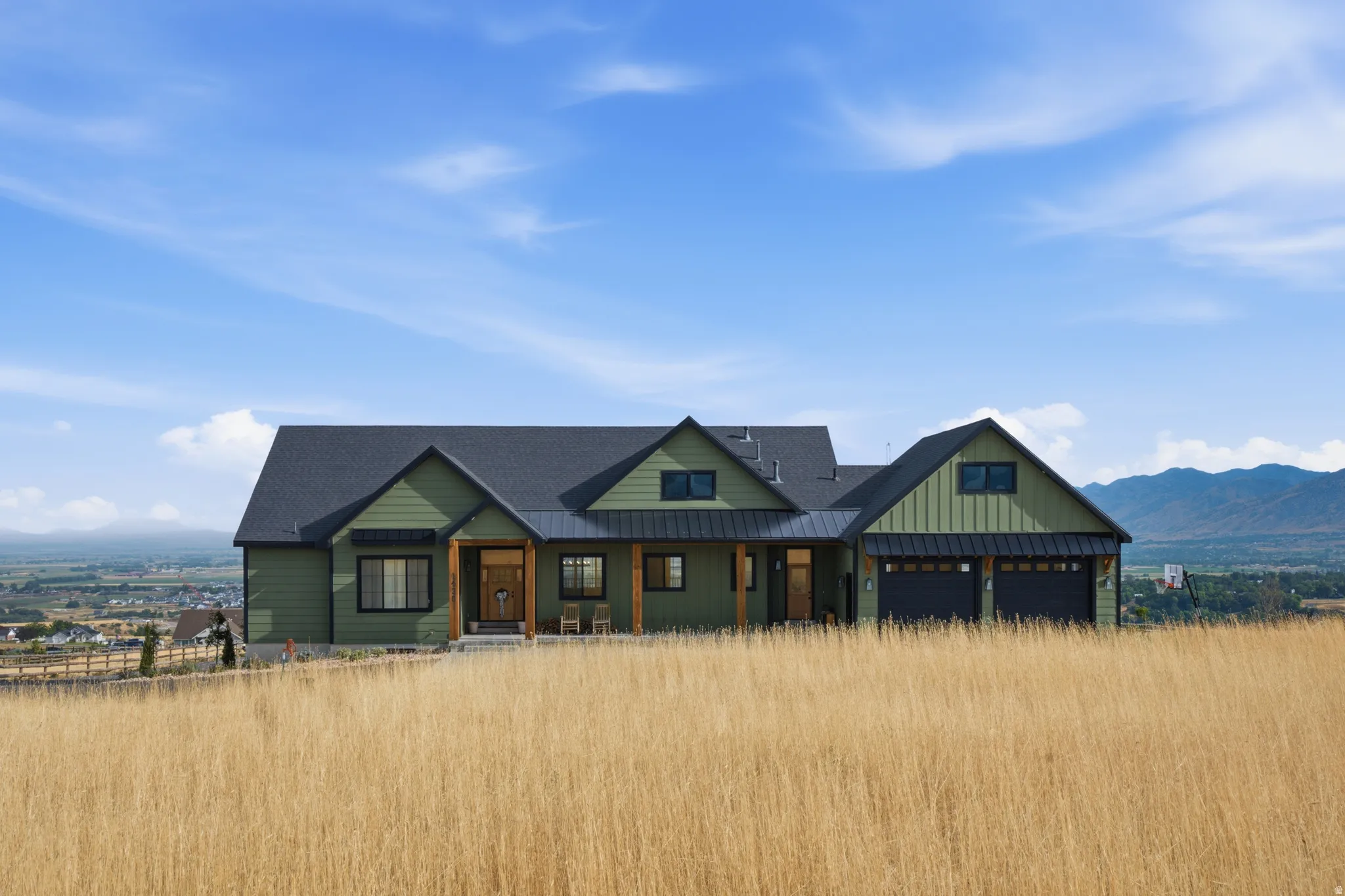 Modern farmhouse exterior with green siding, a dark roof, a two-car garage, and natural wood accents