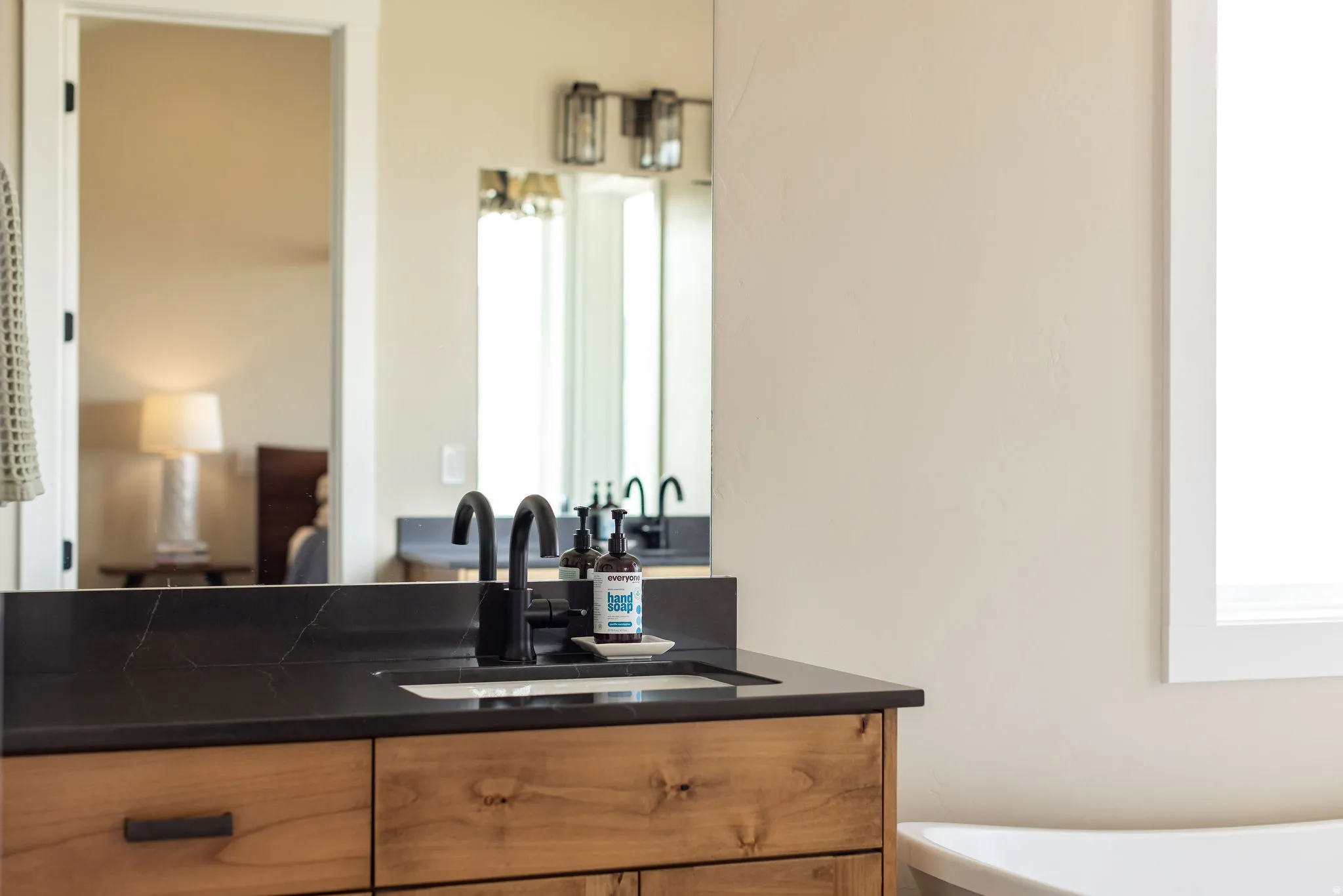 Wood-finish vanity with black countertop, integrated sink, and matte black faucet