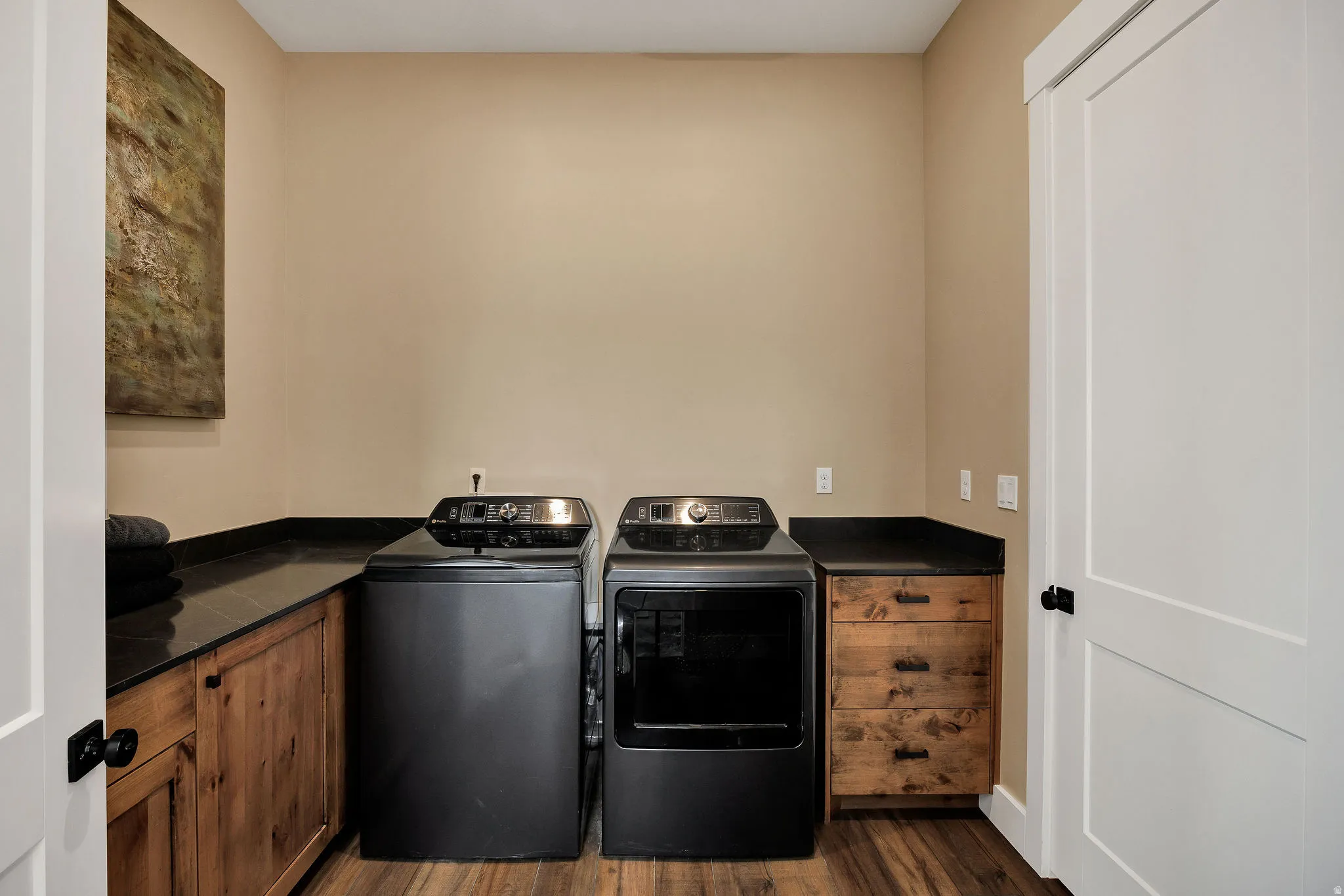 Functional laundry area with wood-finish flooring, dark countertops, and built-in wood cabinetry