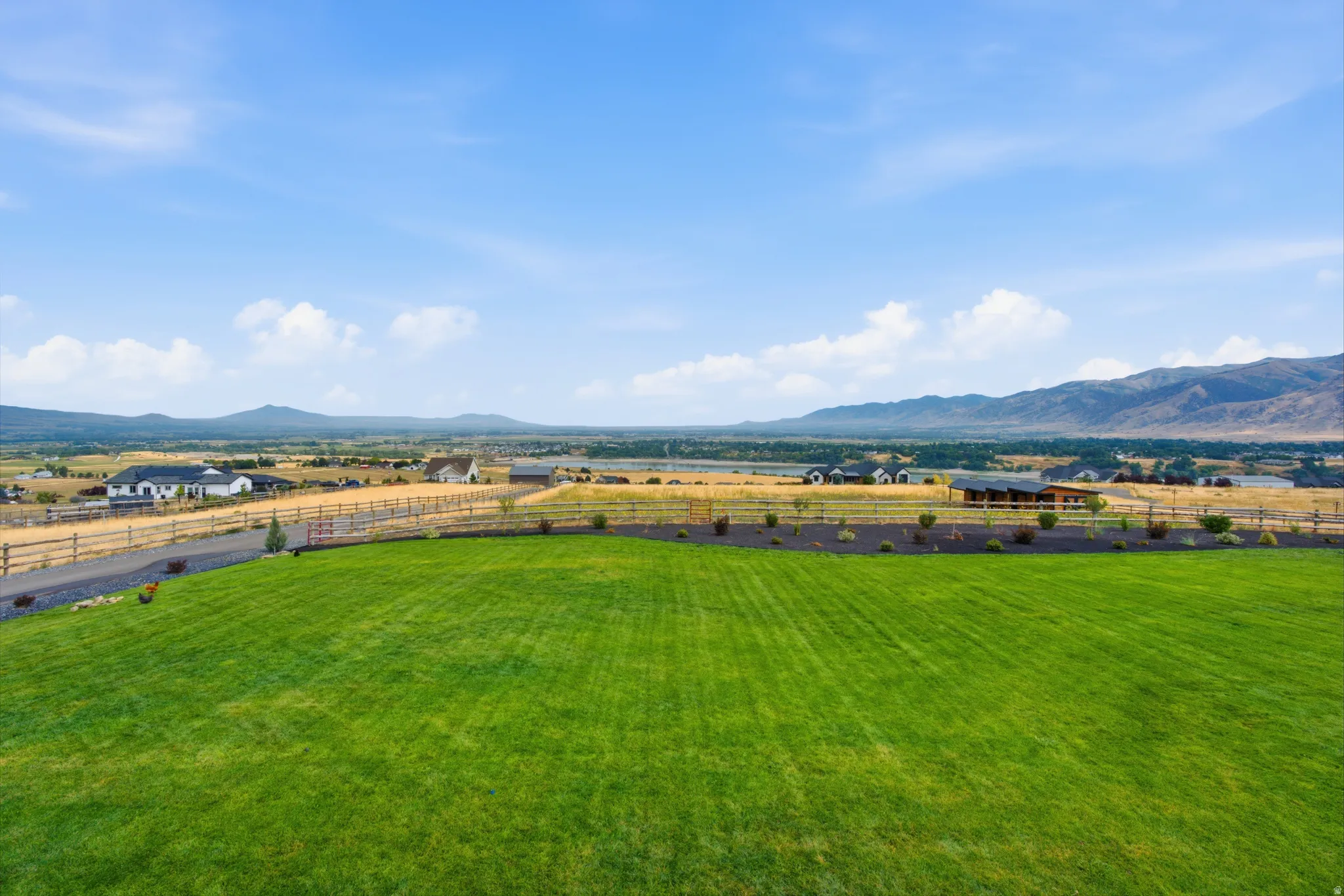 Expansive green lawn with a perimeter fence, gravel driveway, and distant mountain range