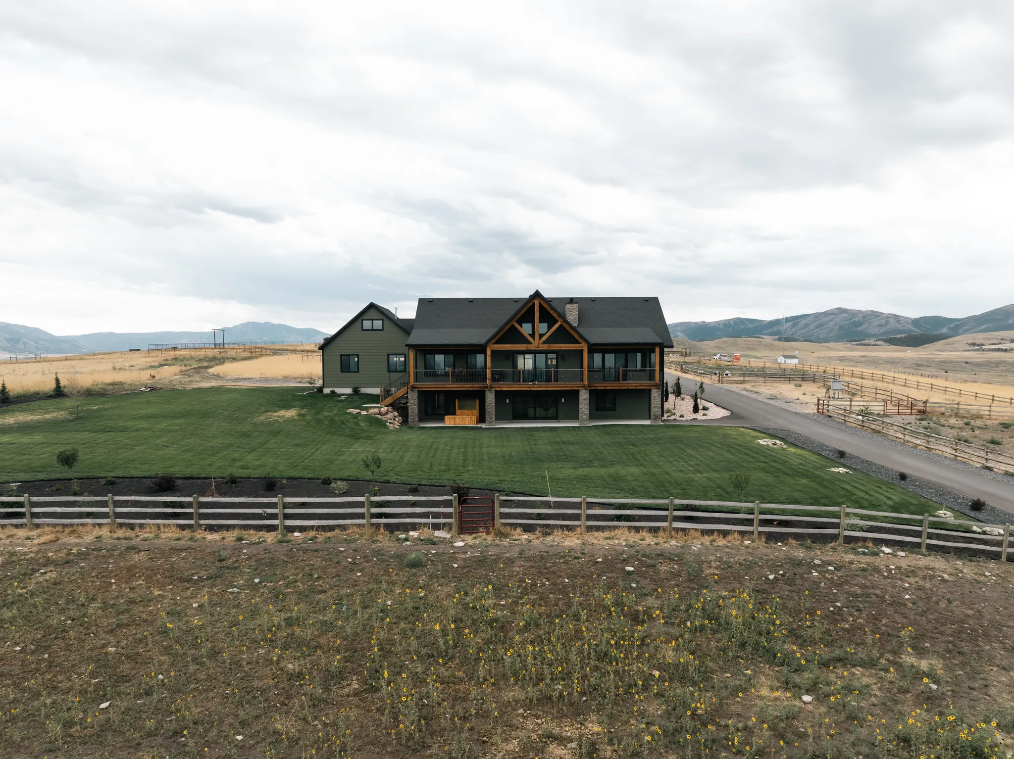 Modern farmhouse residence showcasing a striking dark exterior with mixed material detailing, expansive multi-level design with prominent gabled rooflines, and manicured grounds anchored by white ranch-style fencing