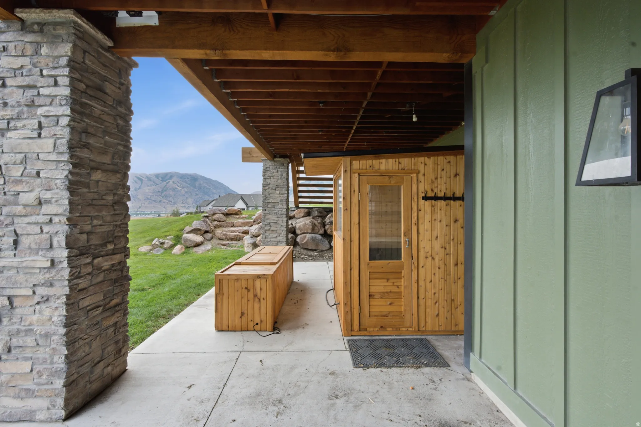 Covered outdoor patio with stone columns, exposed wood beam ceiling, concrete flooring, and a built-in wood sauna