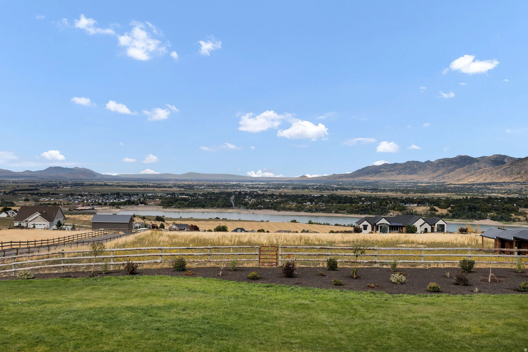 Expansive green lawn with mountain backdrop, split-rail fencing, and distant water feature