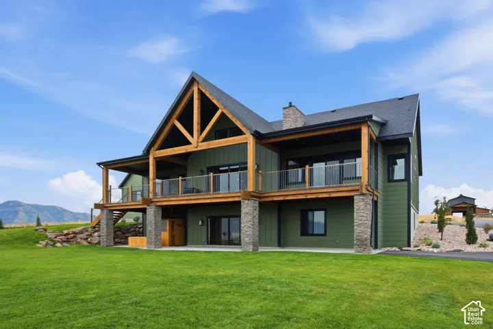 Expansive green siding home with a dark shingled roof, exposed timber framing, stone column accents, and multiple upper-level balconies