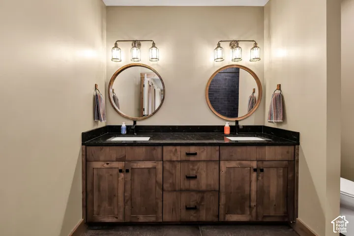 Dual wood-finish vanities with black countertops, integrated sinks, and individual round mirrors with sconce lighting
