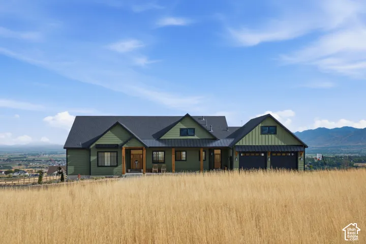 Modern farmhouse exterior with green siding, a dark roof, a two-car garage, and natural wood accents