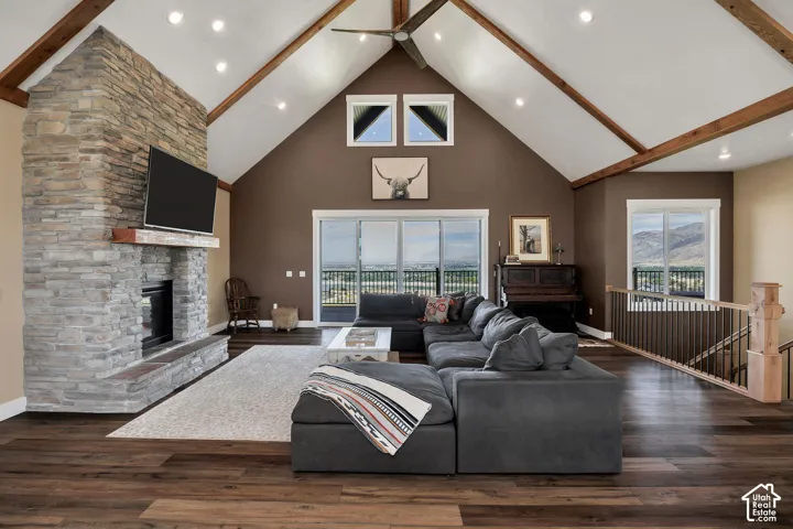 Vaulted ceiling with exposed wood beams, stone-clad fireplace with hearth, wood-finish flooring, and sliding glass doors to a balcony