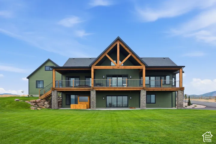 Expansive green lawn with a two-story residence featuring a covered deck, substantial timber frame elements, and stone-clad structural supports