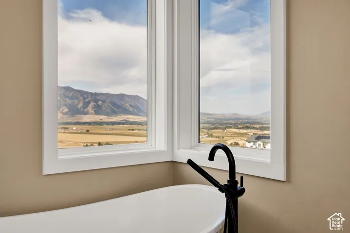 Freestanding soaking tub with floor-mounted matte black faucet, set against expansive mountain and valley scenery