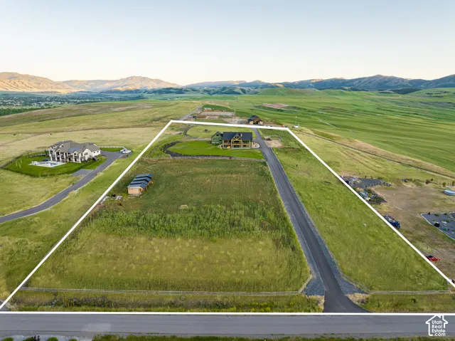 Expansive land parcel featuring a paved road, mountain backdrop, and surrounding green spaces