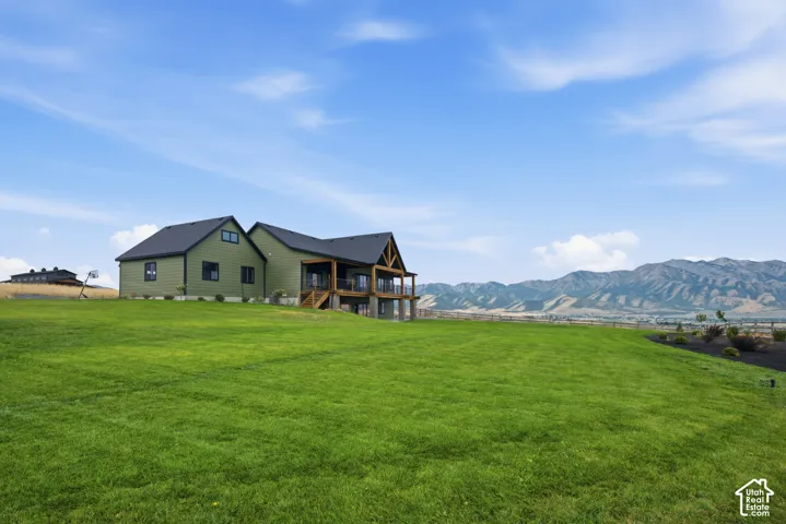 Expansive green lawn surrounding a residence with a covered deck, dark siding, and a prominent mountain range backdrop