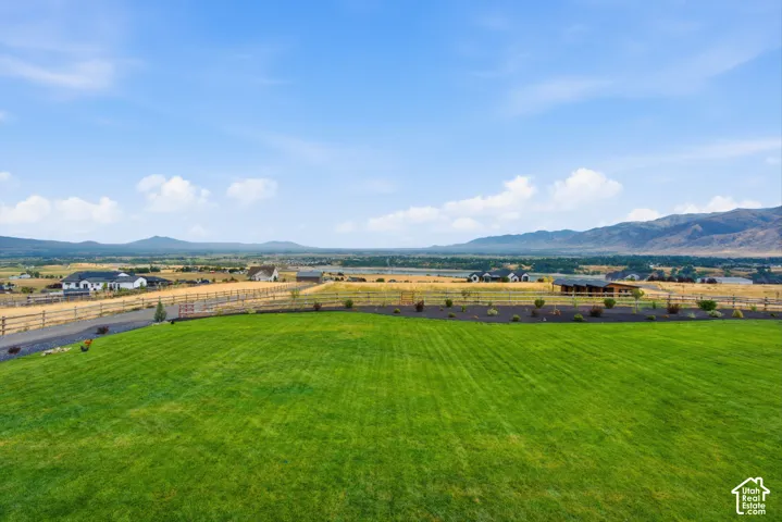 Expansive green lawn with a perimeter fence, gravel driveway, and distant mountain range
