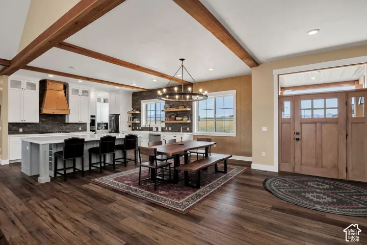 Wood-finish flooring throughout, a kitchen island with seating, exposed ceiling beams, a wood-paneled front door with side panels, and white cabinetry