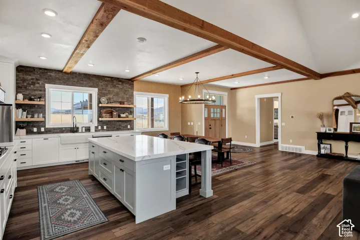 Gourmet kitchen with a large island, white shaker cabinetry, farm sink, and exposed wood beams