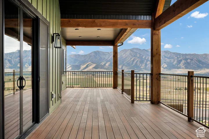 Expansive outdoor deck with wood-finish flooring, black metal and glass panel railing, exposed timber beams, and sliding glass doors