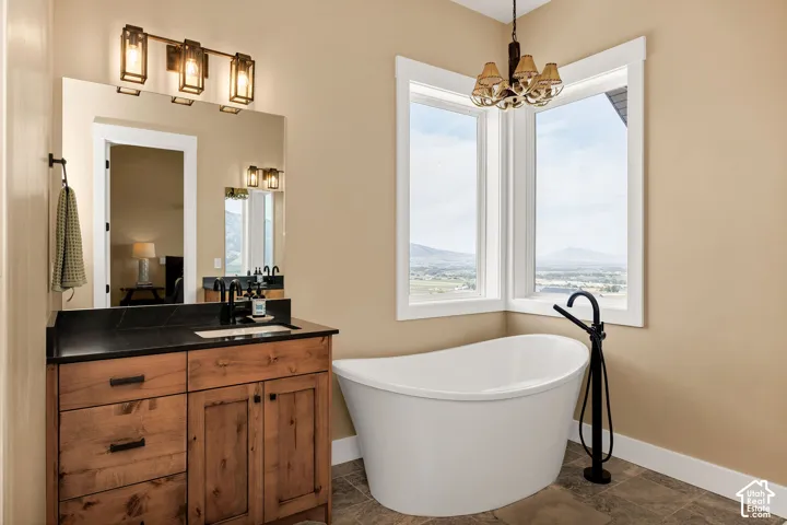 Freestanding soaking tub with floor-mounted fixture, wood-finish vanity with dark countertop, large vanity mirror, and corner windows