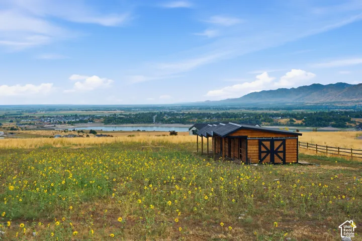 Wood-clad outbuilding with covered stalls and a sliding barn door, set amidst a sprawling field