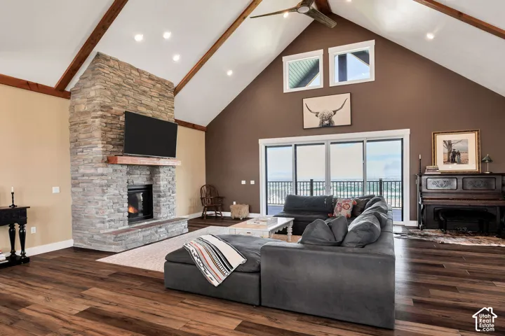 Vaulted ceiling with exposed wood beams, stone fireplace, wood-finish flooring, recessed lighting, and expansive sliding glass doors