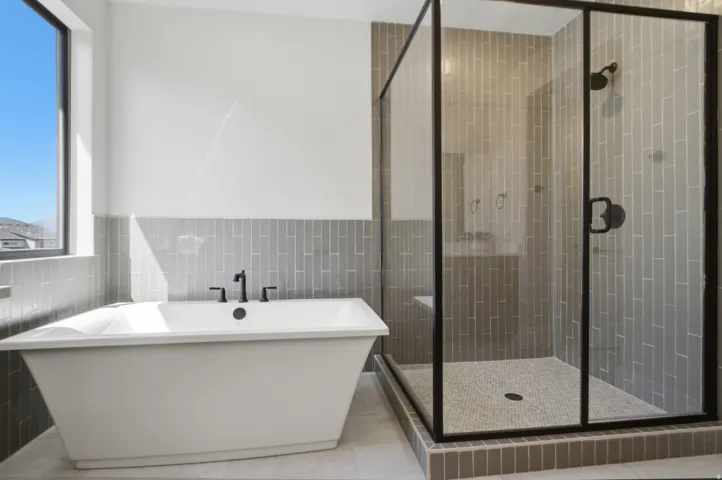 Freestanding soaking tub with matte black fixtures, glass-enclosed shower with subway tile surround, patterned tile shower floor, and a large window