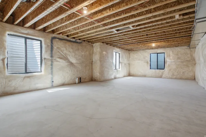 Unfinished basement with concrete flooring, exposed ceiling joists, and insulated walls