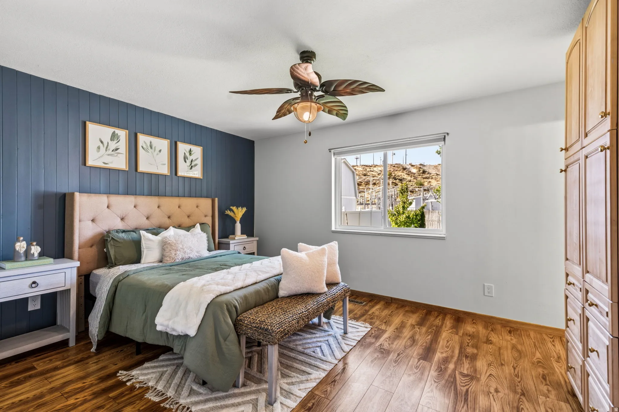 Wood-finish flooring, accent wall with vertical paneling, single window, ceiling fan with light fixture, and built-in cabinetry