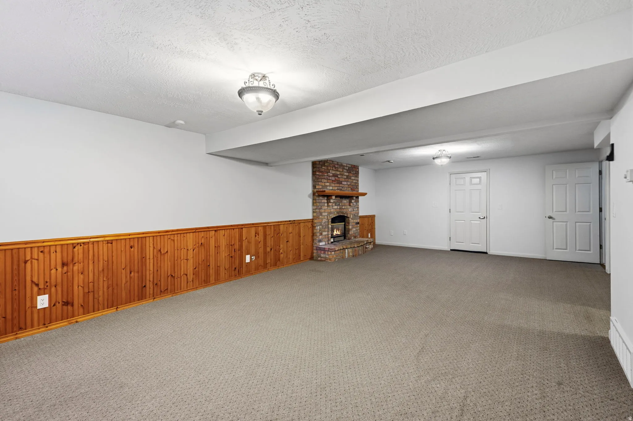 Brick fireplace with wood mantel, wall-to-wall carpeting, wood paneling, and two paneled doors